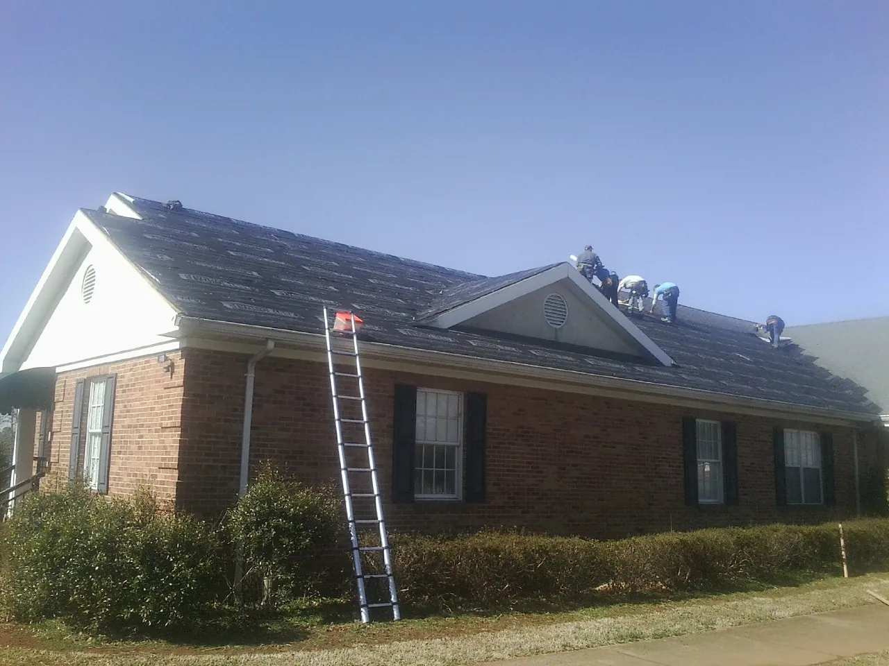 Crew tearing shingles off a brick ranch roof with a ladder set — Emergency Roof Repair work by our crew in Palisade