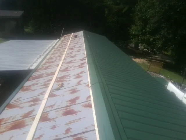Old rusted panels beside newly installed green metal roofing — Wind Damage Roof Repair by Roofing Brothers in Palisade