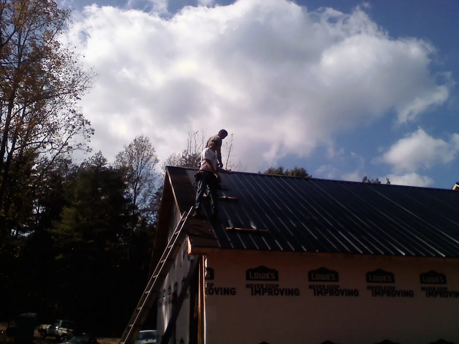 Roofer fastening dark metal panels high against a cloudy sky, from a Roof Inspection job in Palisade