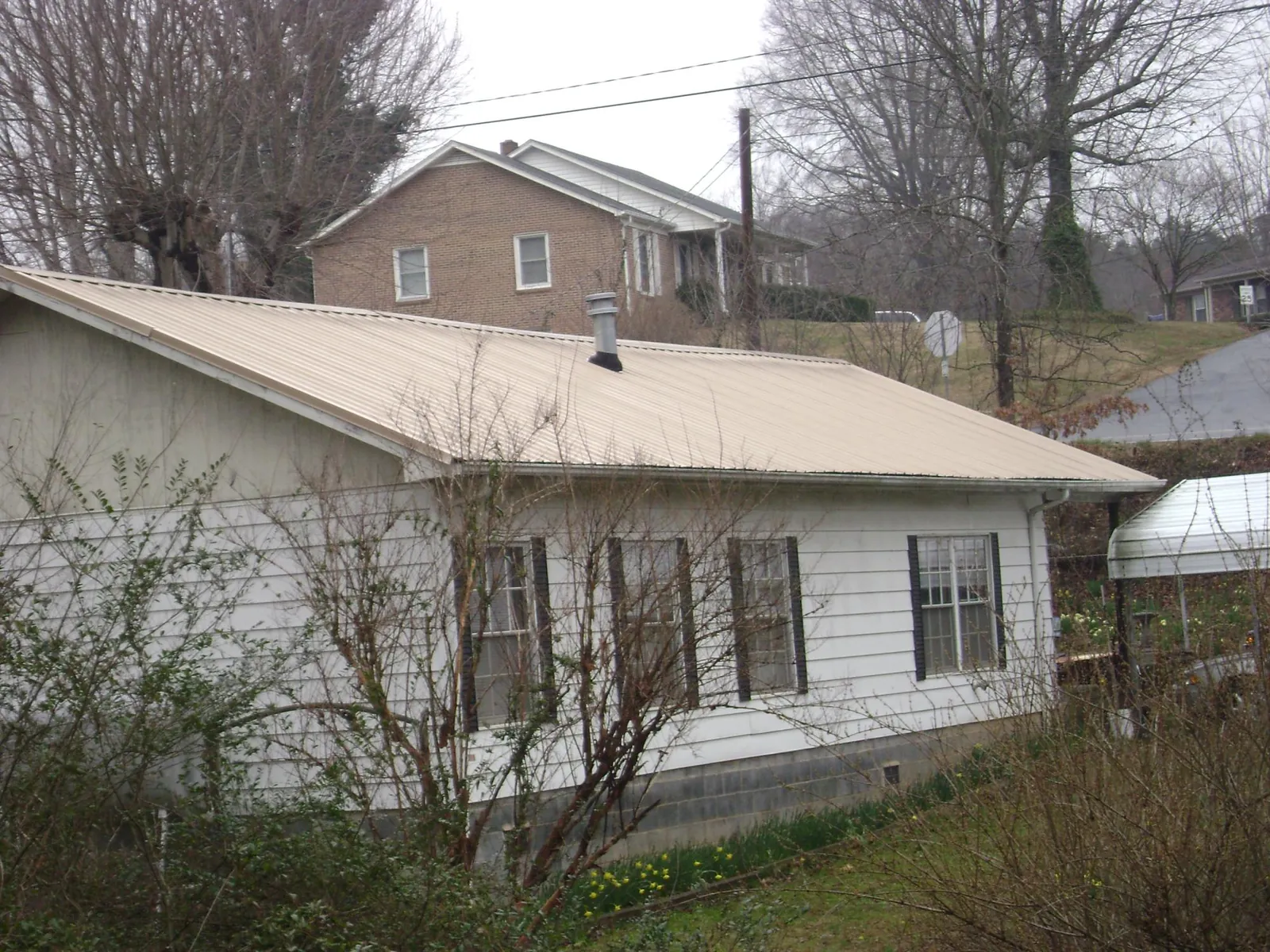 Tan metal roof on a white sided house set into a hillside — Commercial Roofing by Roofing Brothers in Palisade